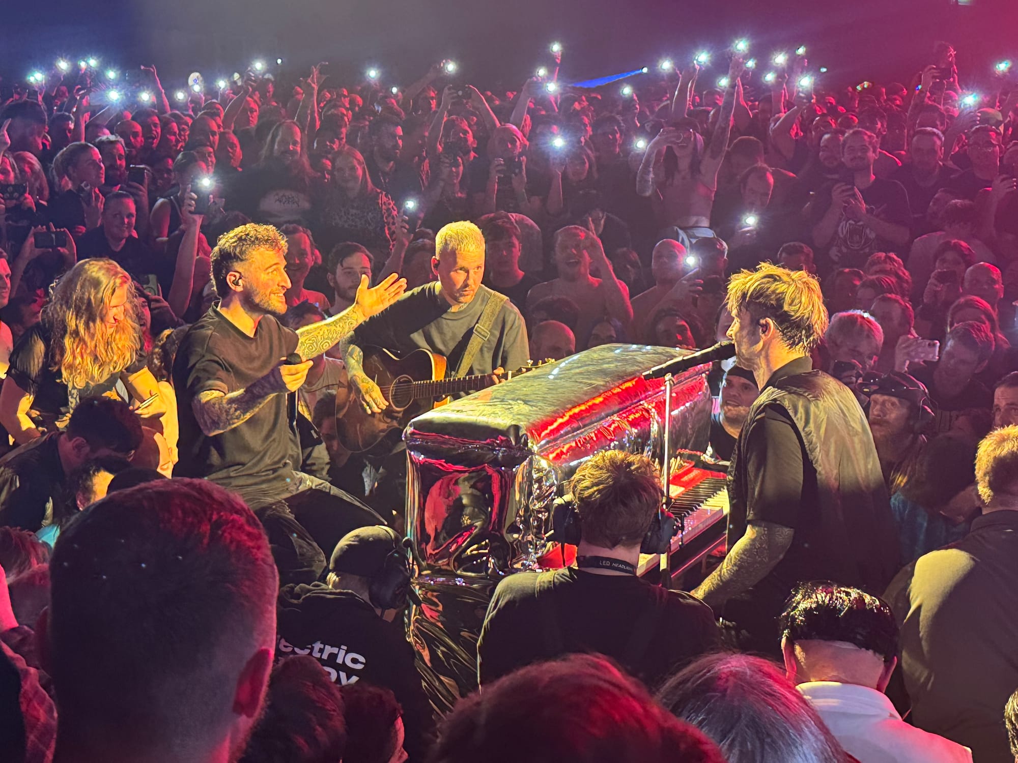 Nico, Danskimo, and Kevin in the middle of the crowd with a piano and acoustic guitar. medium-shot.